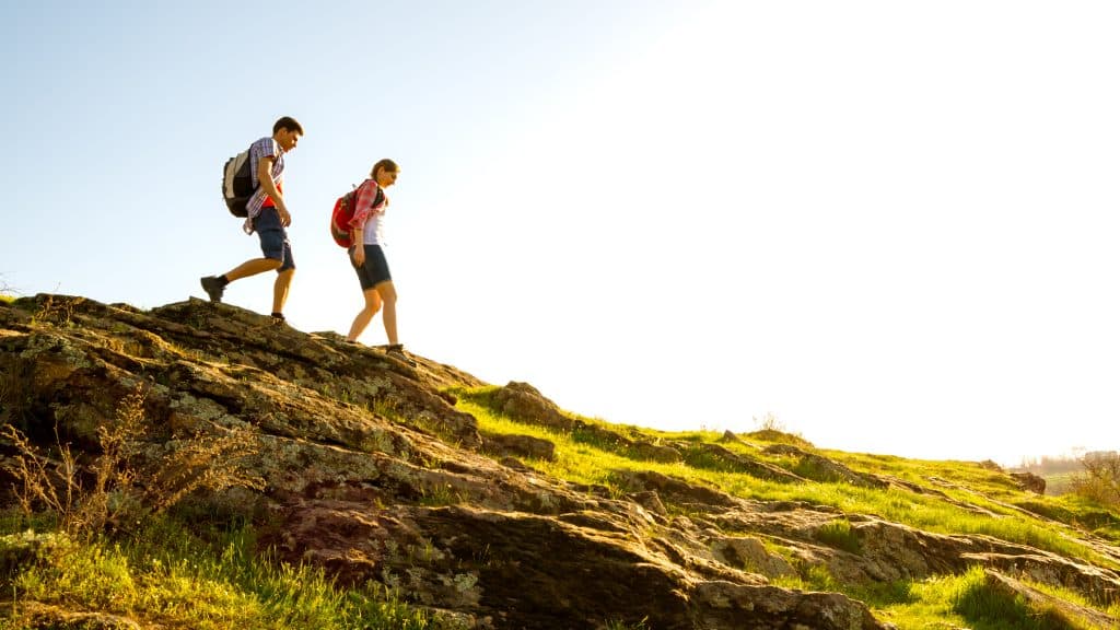 Image shows two people hiking down a gradual decline alongside a hill.