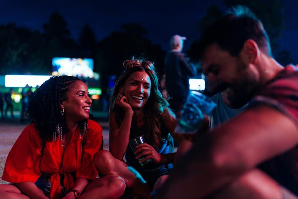 Image shows a group of young adults, sitting at what looks to be a fair or carnival. People enjoying company of each other.