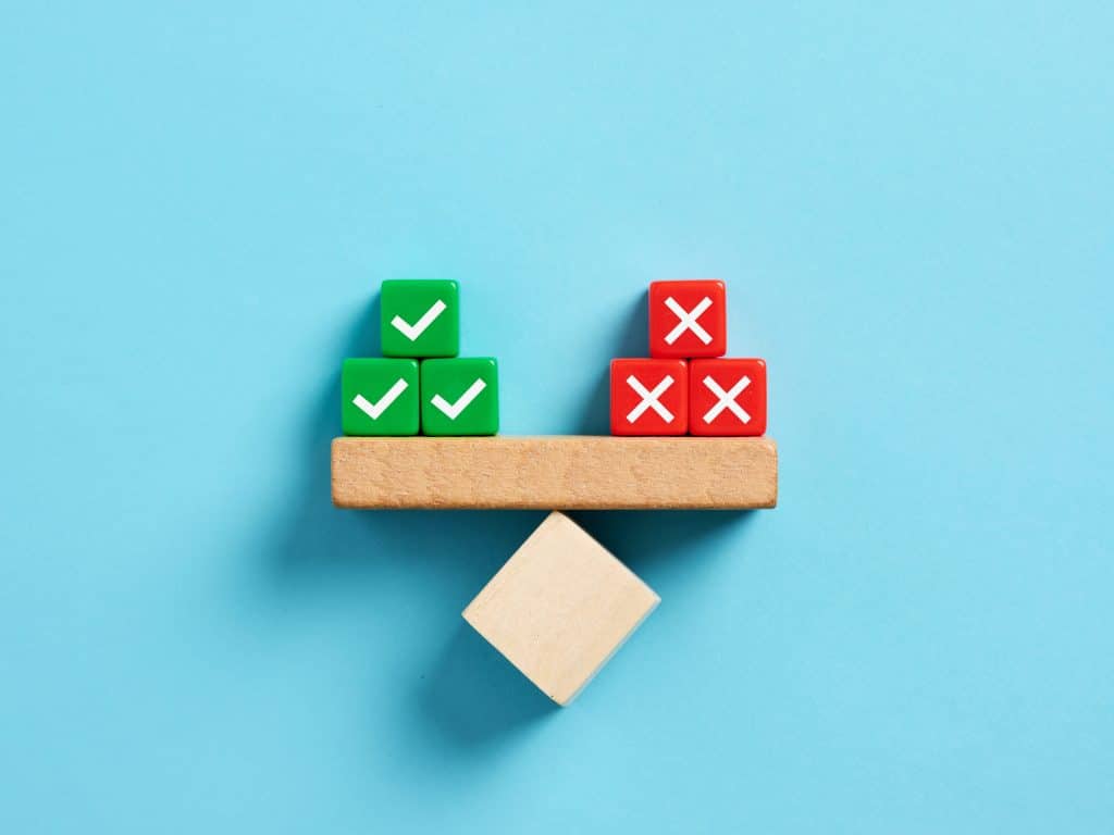 Three dice blocks marked positive and negative balancing on a wooden seesaw