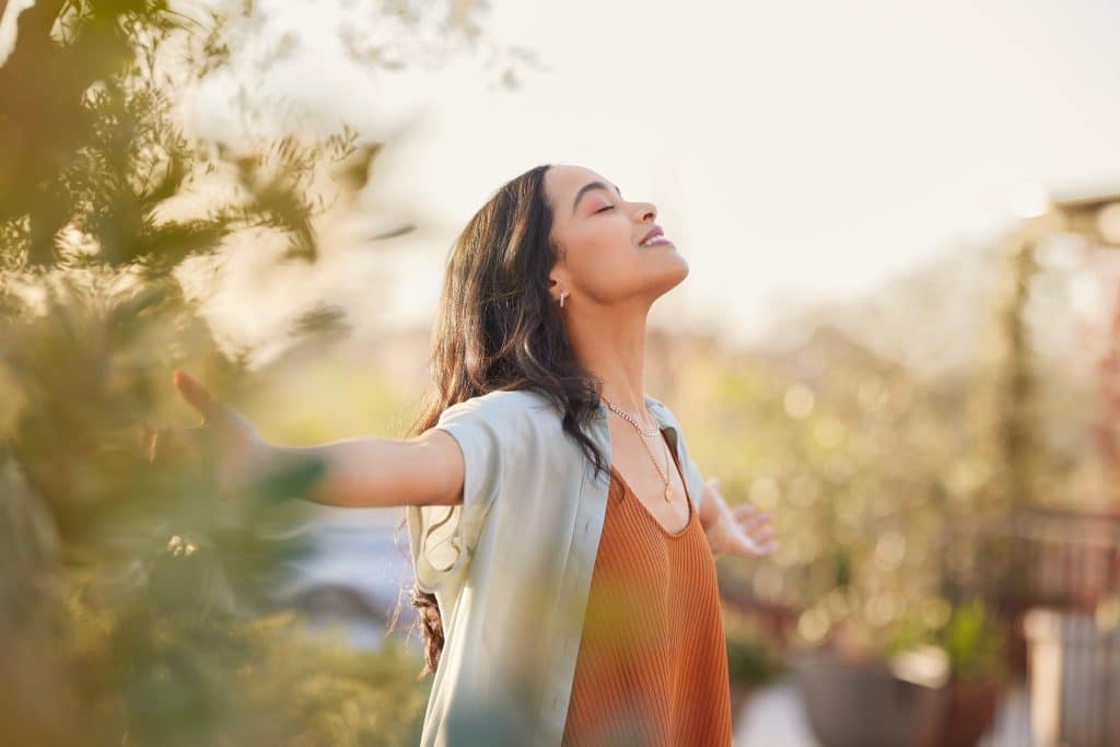 Image shows woman with arms outstretched, breathing in fresh air amongst greenery