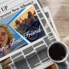 A newspaper with the headline "What's up with Sabrina Carpenter new album?" and a picture of Sabrina sits on a desk with a steaming coffee cup.