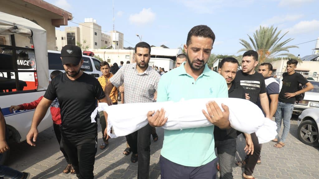 Palestinians carry the body of a 3-year-old child, Amir Qanan, who was killed after an Israeli air strike on his home. Shutterstock/Anas Mohammed
