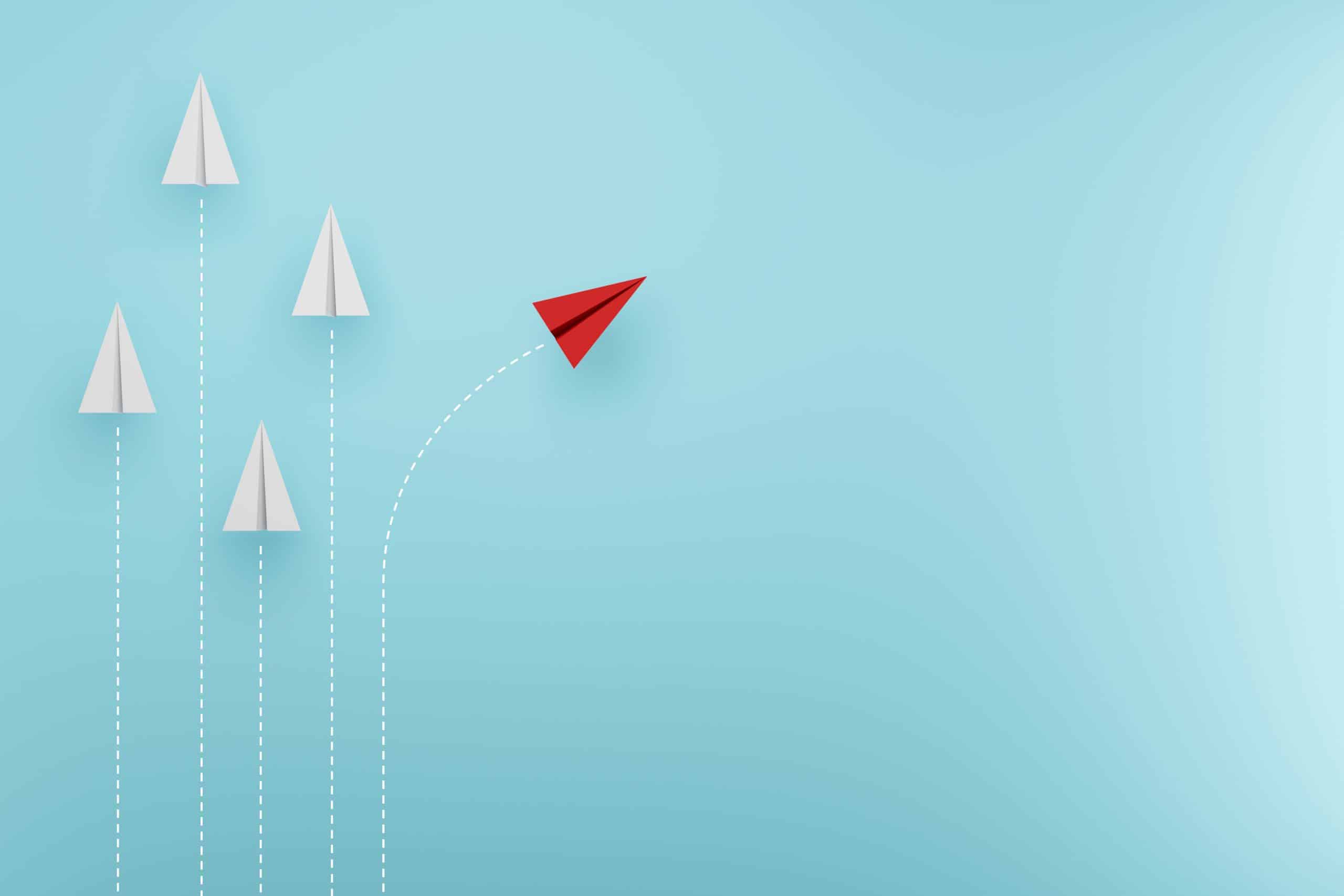 A group of white paper airplanes flying straight while one red paper airplane flies right