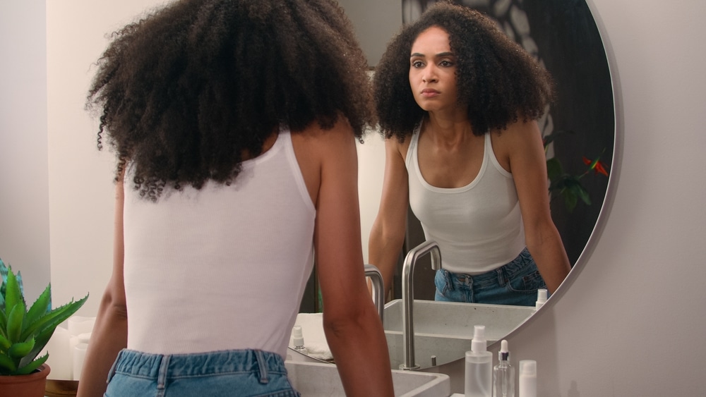 A woman looks into a mirror above her bathroom sink, considering what she sees. Change is hard.