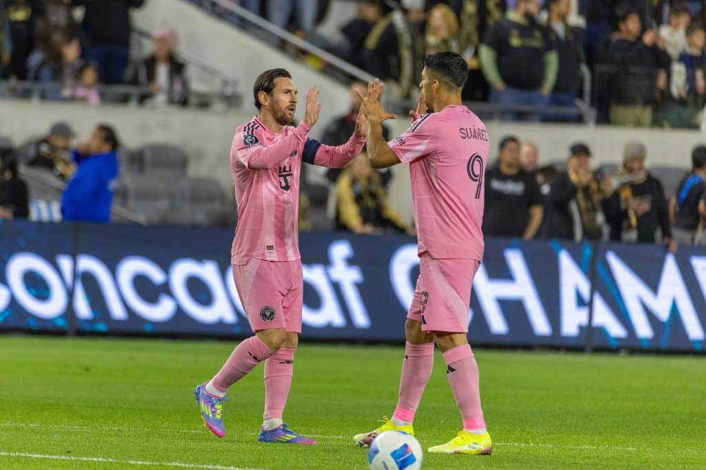 Inter Miami teammates Lionel Messi and Luis Suarez high five on the pitch.