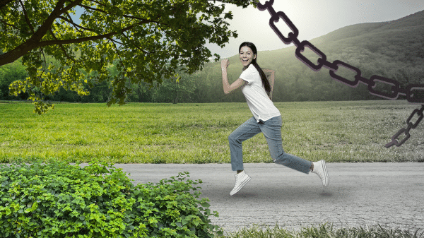 A woman escaping from a grey, chain-filled area. Running towards the bright green grass with a big smile on her face.