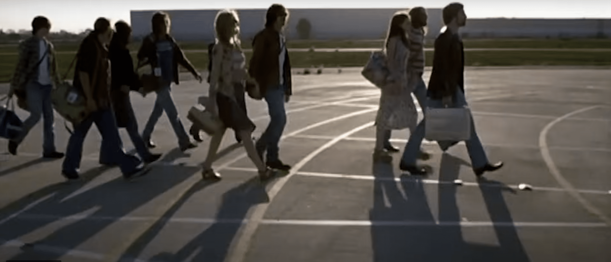 Group of bandmates walking together outside carrying luggage.