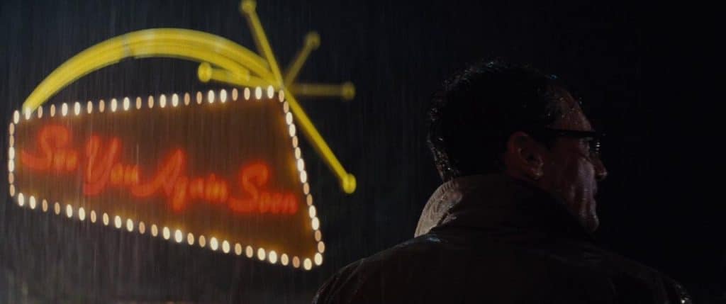 John Hamm's Character Laramie Seymour Sullivan again backlit by a neon sign in the rain, this one reading See You Again Soon.