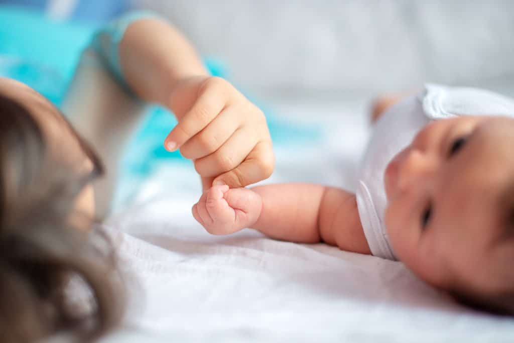 Newborn baby with her older sister together on the bed holding each other`s hand. (Shutterstock/ Pazargic Liviu)