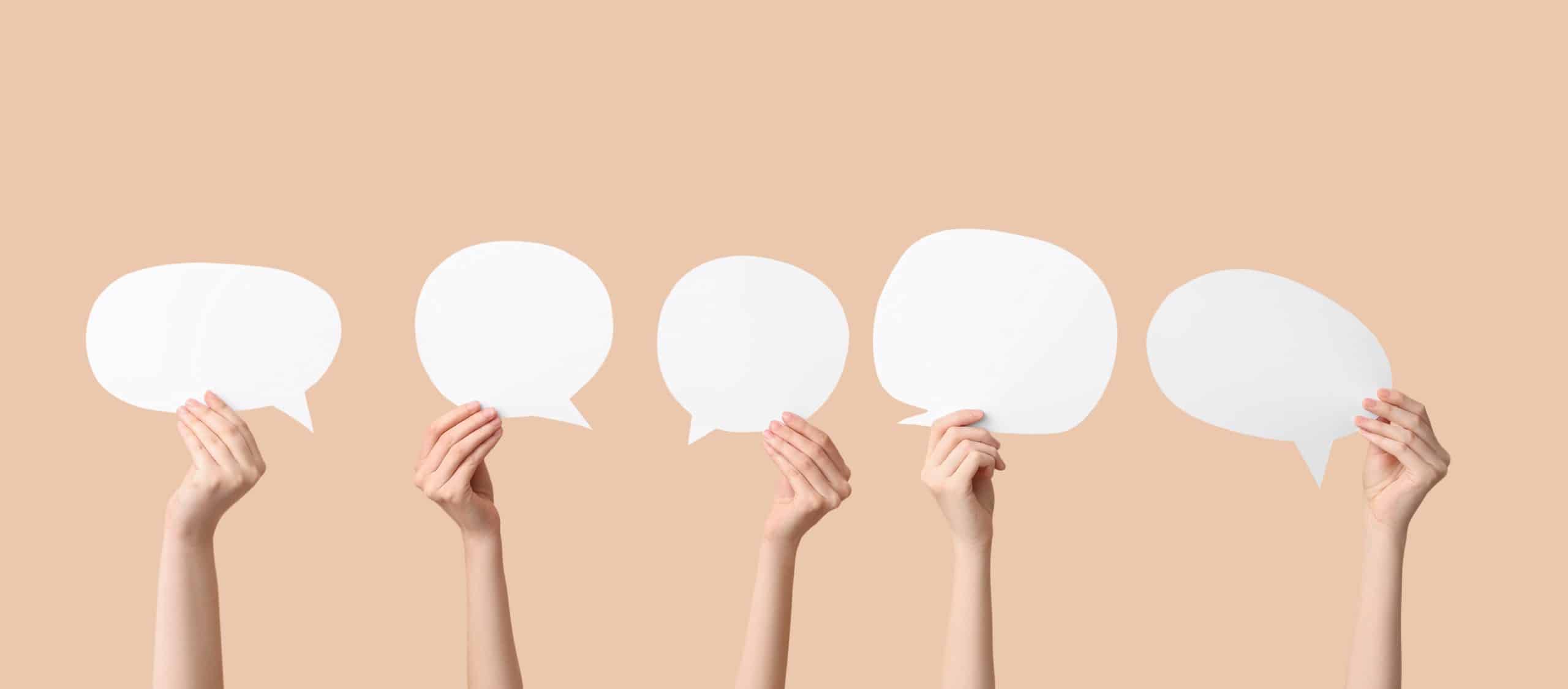 Hands with blank speech bubbles on beige background. (Shutterstock/ Pixel-Shot)