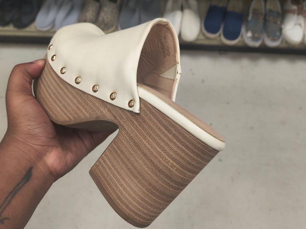 A heeled shoe with a white top, gold grommets, and a brown heel in a thrift store.