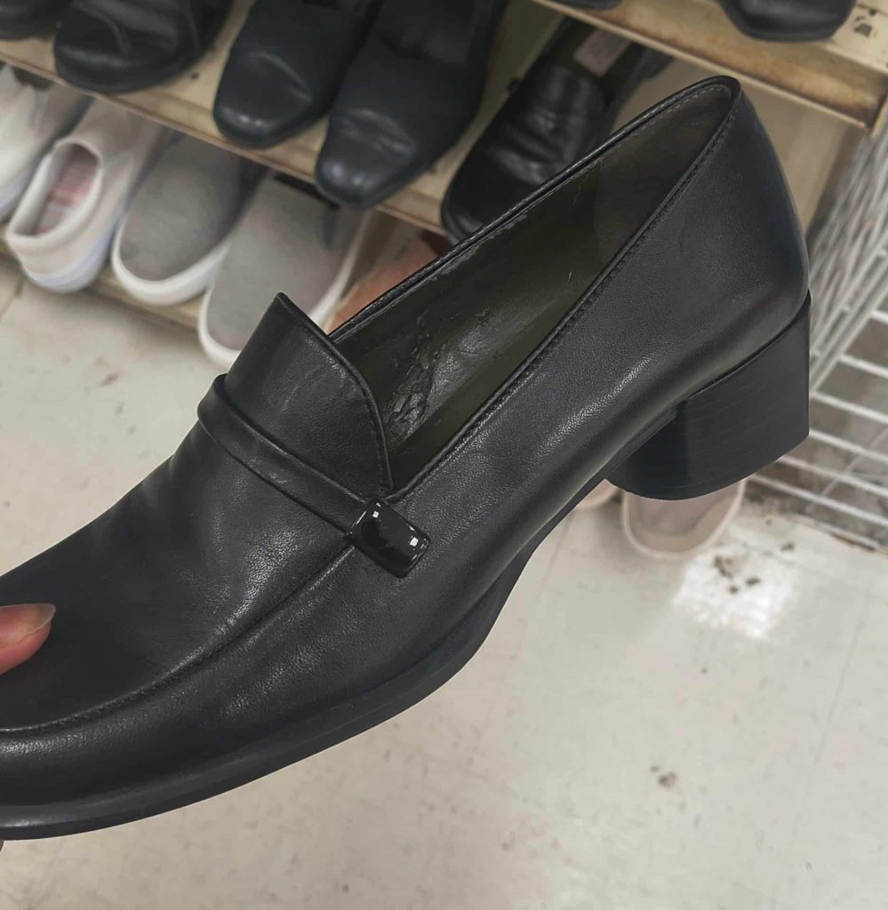 A black loafer shoe in a thrift store with shoes on shelves in the background.