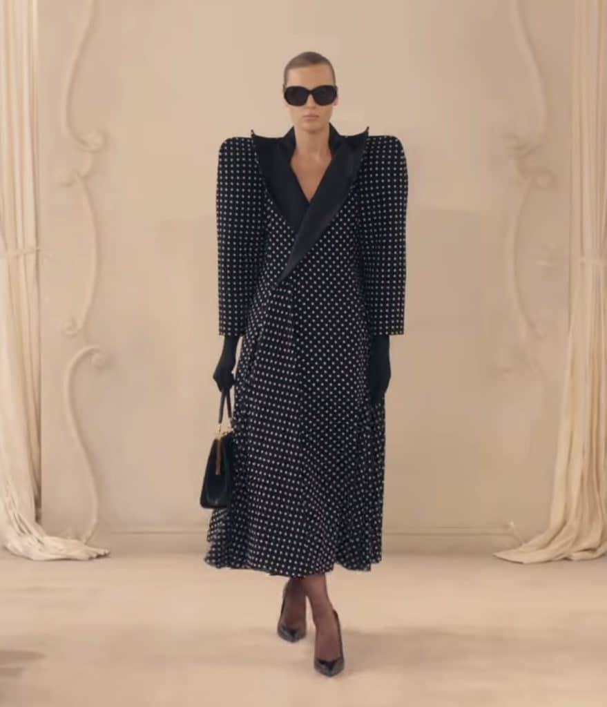 A model walks down the Balenciaga runway in a coat that also functions as a dress, with a polka dot pattern.