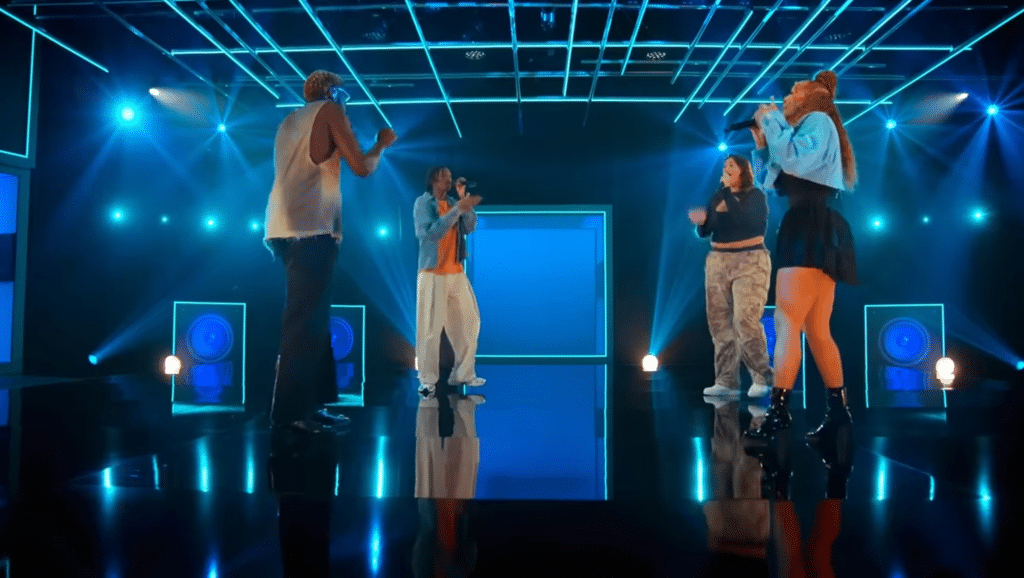 4 people on a stage singing together.