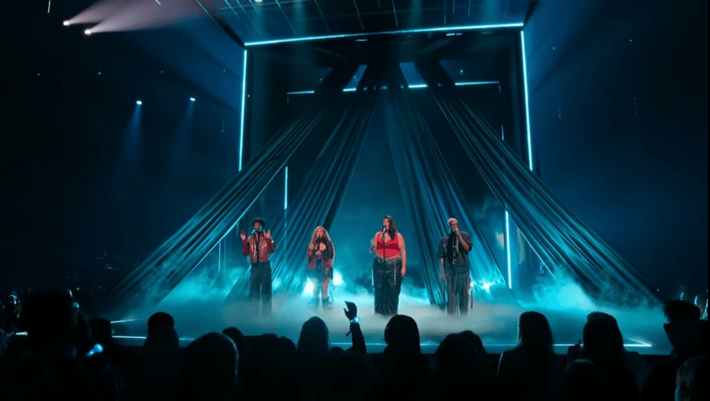 Four people singing on stage with strobe lighting.