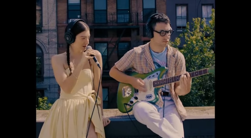 Jack Antonoff playing guitar while Lorde sings on a rooftop.