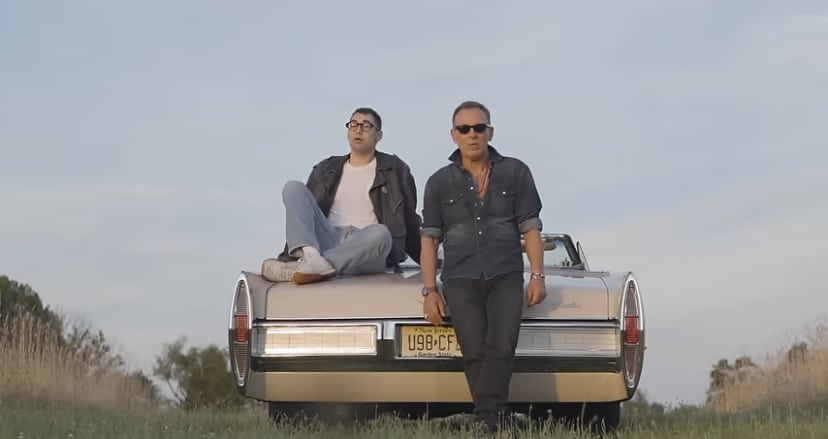 Jack Antonoff and Bruce Springsteen sitting on a car in the desert.