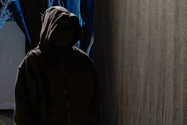Person in dark clothing hiding away in dark lighting: Mystery villain.