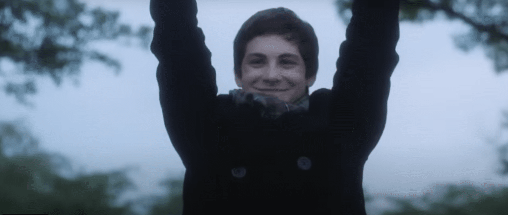 Boy wearing coat, holding his arms up, smiling.