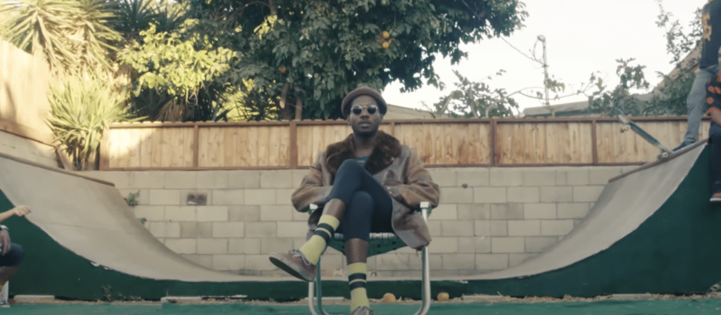 Still from Channel Tres music video, he's sitting in a chair in front of a half pipe
