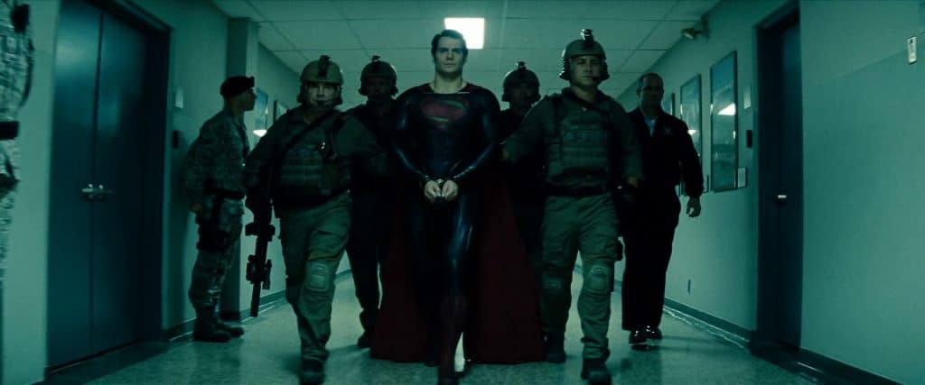 Superman being escorted down a dimly-lit hallway after being arrested.