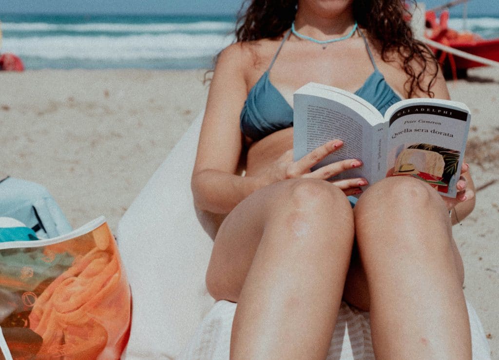 A woman reading a book by the beach.