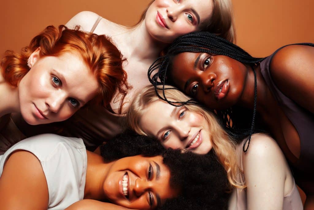 young pretty african and caucasian women posing cheerful together on brown background, lifestyle diverse nationality people concept