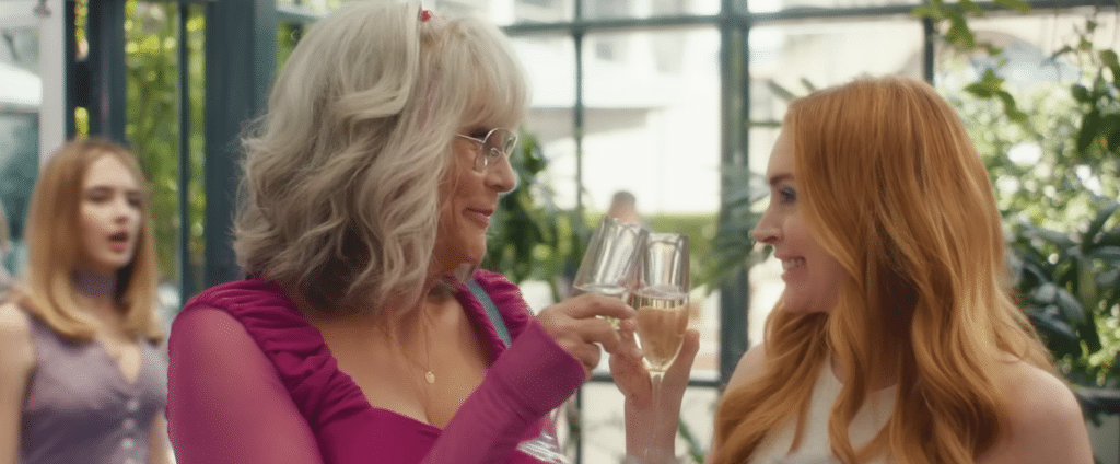 Two women clink champagne flutes while a teenage girl watches from a distance.