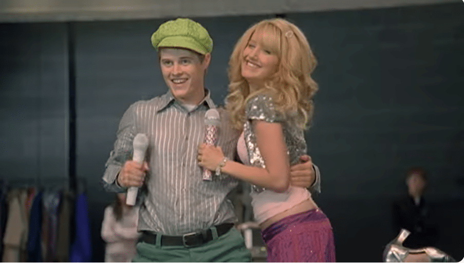 A brother and sister duo stand on stage holding microphones and hugging each other.