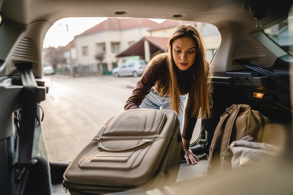 A female moving to college lifts her luggage out of her car.