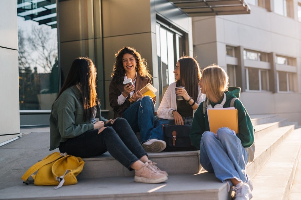 Four college friends sit on the steps of their university.
