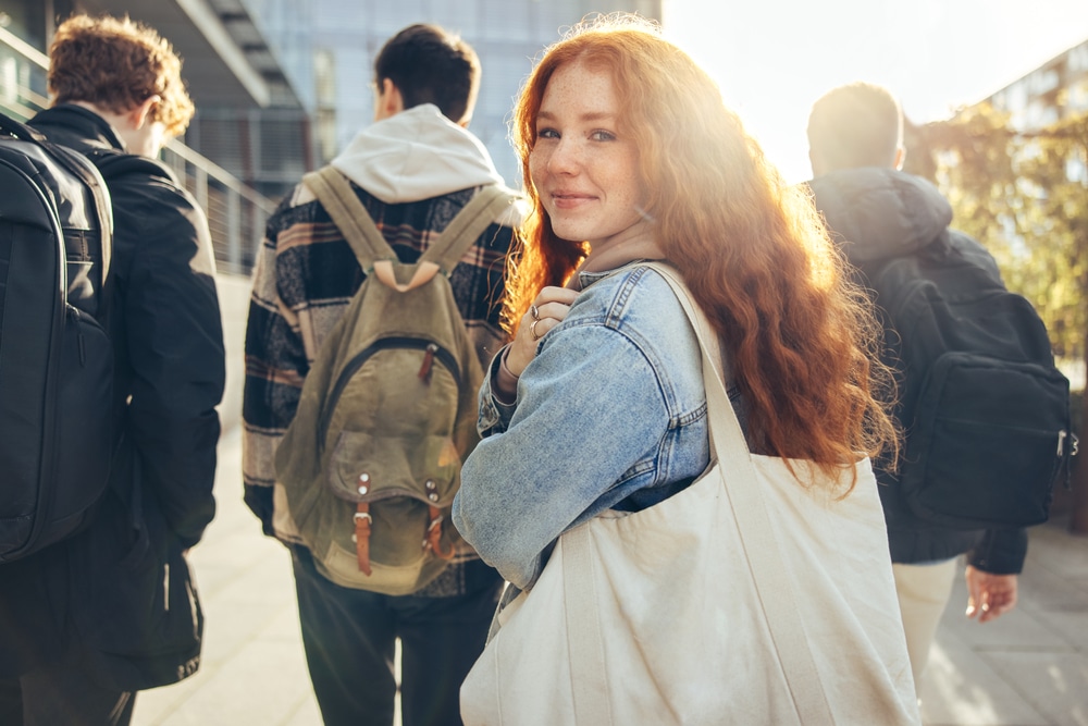 Female college student surrounded by friends walks forward, smiling back at the camera