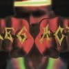 Close-up of two fists with the word ‘LEGACY’ tattooed across the knuckles in bold gold letters, with a blurred basketball court background and a player wearing a headband in the distance.