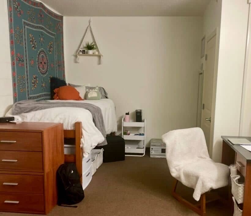 one side of dorm room featuring bed, dresser, and desk chair