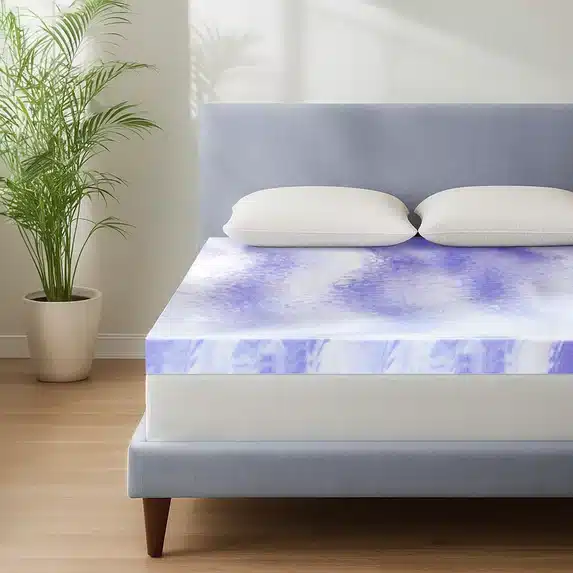 A bedroom with a plant on the left side and a bed on the right side. There are two white pillows and a purple and white mattress topper on the bed.