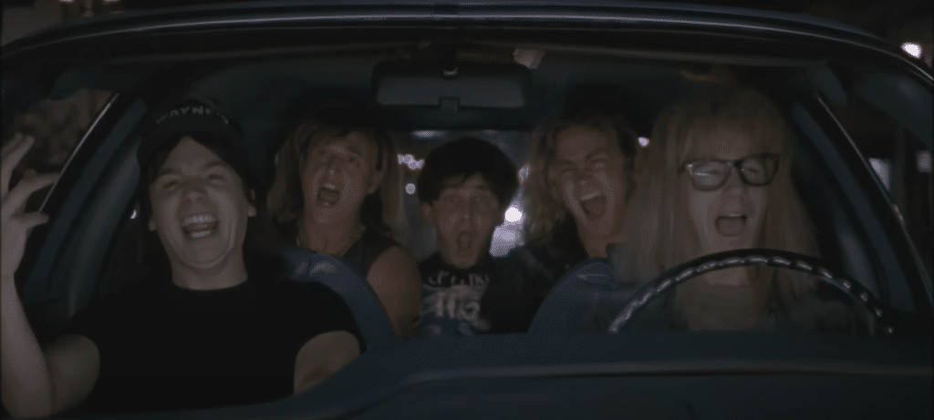 Wayne, Garth, and Three friends sit in car singing.