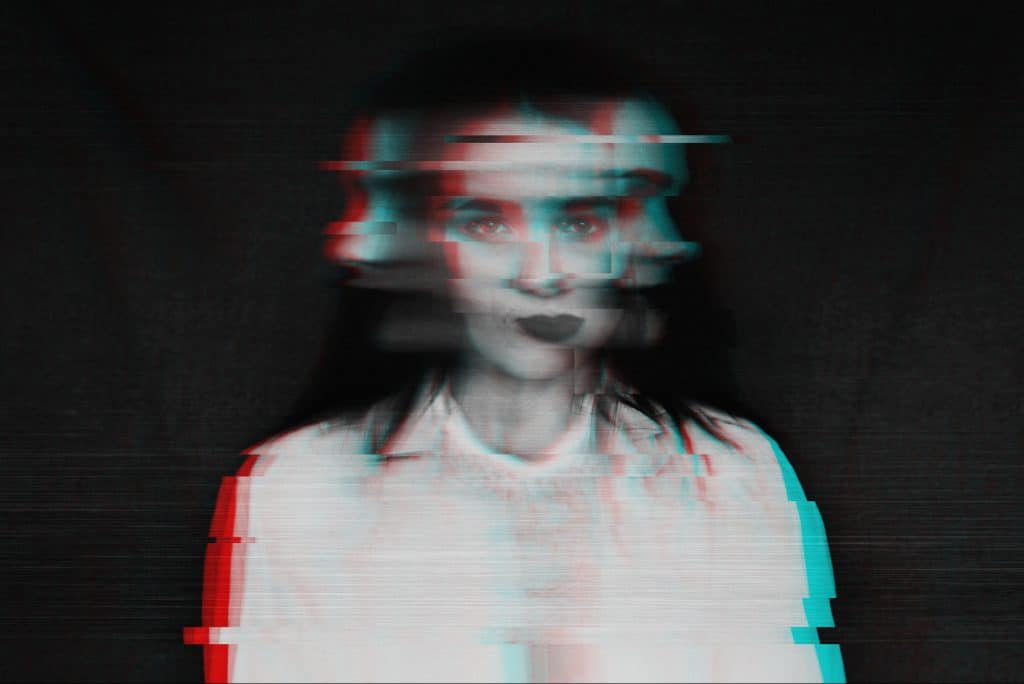 A portrait of a woman in black and white with an ambigious expression, whose image is distorted with red and blue computer glitch-like affects.