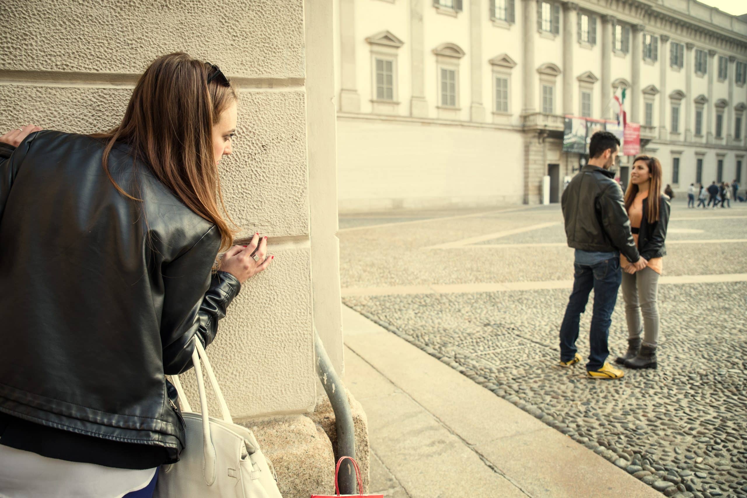 A woman peeks at a couple behind a wall.