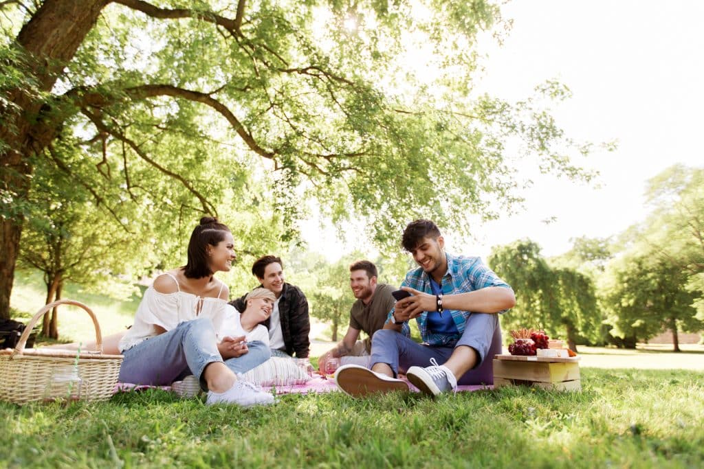 Friends chill outside on a picnic blanket in the sun.