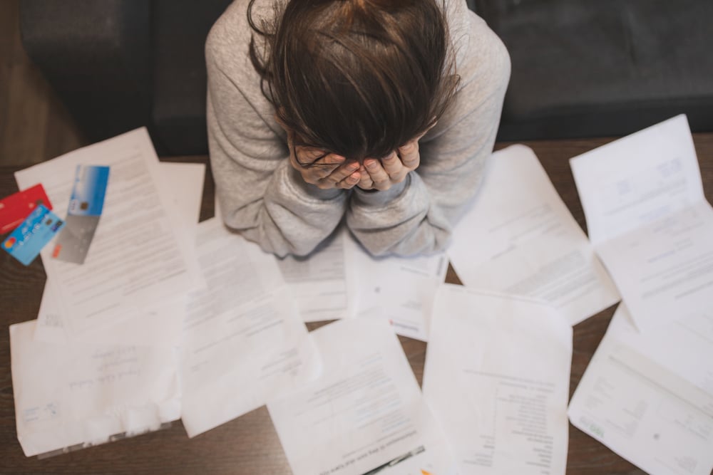 female student with her head in her hands, stressed about all the work she has to do to with a bunch of papers spread on her desk.