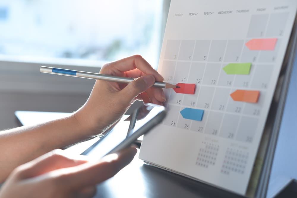 a hand holding a phone while filling in a calendar