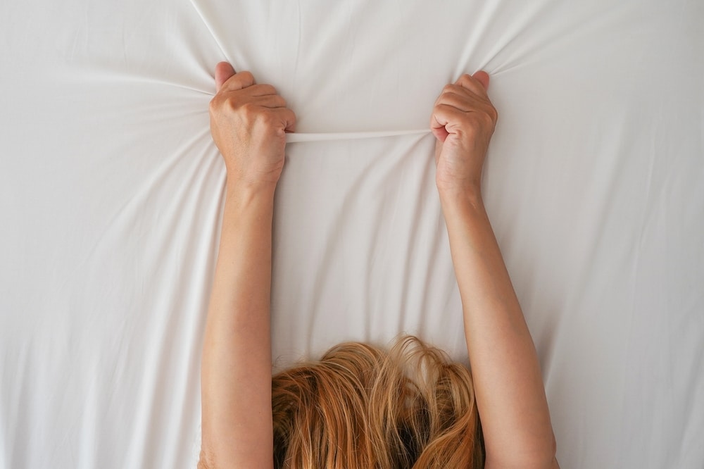 A woman clutches the sheets.