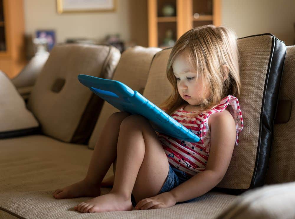 meet the zillennials A blonde girl, toddler-aged, staring at a blue tablet on her lap.