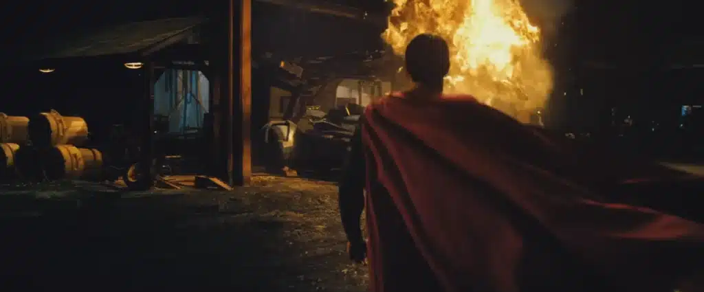 Superman, with cape fluttering, walking towards an explosion.