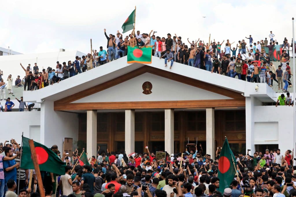 Hundreds of people waving the Bangladesh flag on top of and below the parliament building in Dhaka, Bangladesh.