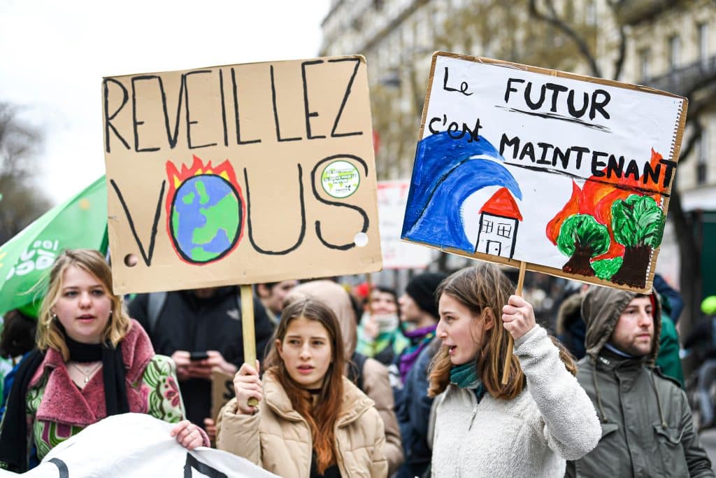 Young climate protesters holding up signs reading "wake up" and "the future is now" in Paris, March 2023.
