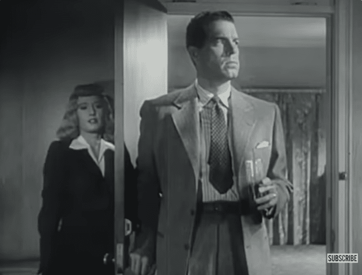 A woman hiding behind a door watches a man in a suit.