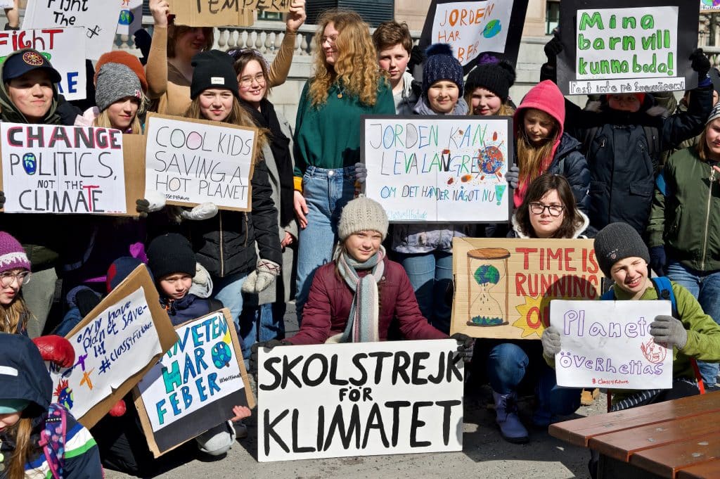 Greta Thunberg protesting with tens of other people in Sweden. All holding signs asking for governments to fight against climate change.