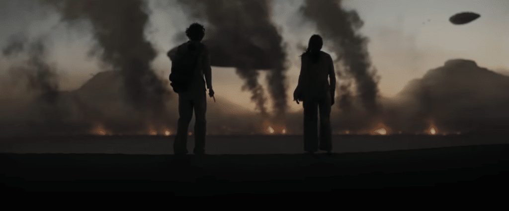 Man and woman stand looking at the landscape on fire.