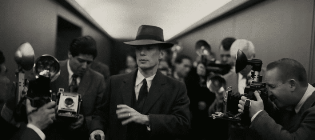 Man walks down a hallway, surrounded by photographers on both sides of him.